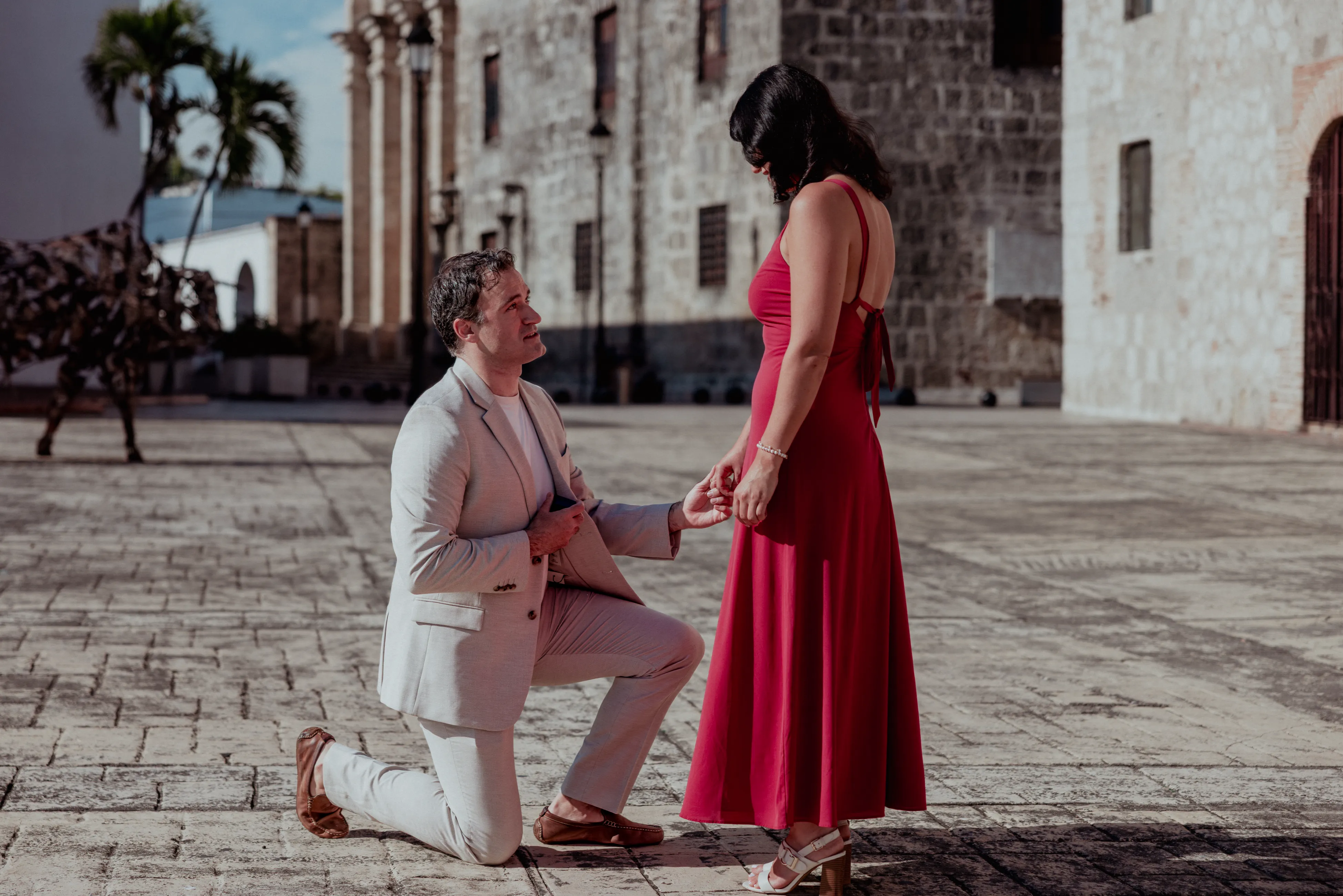 Propuesta de matrimonio en Zona Colonial Hombre en traje blanco arrodillado frente a mujer con vestido rojo en plaza colonial de Santo Domingo, propuesta de matrimonio fotografía