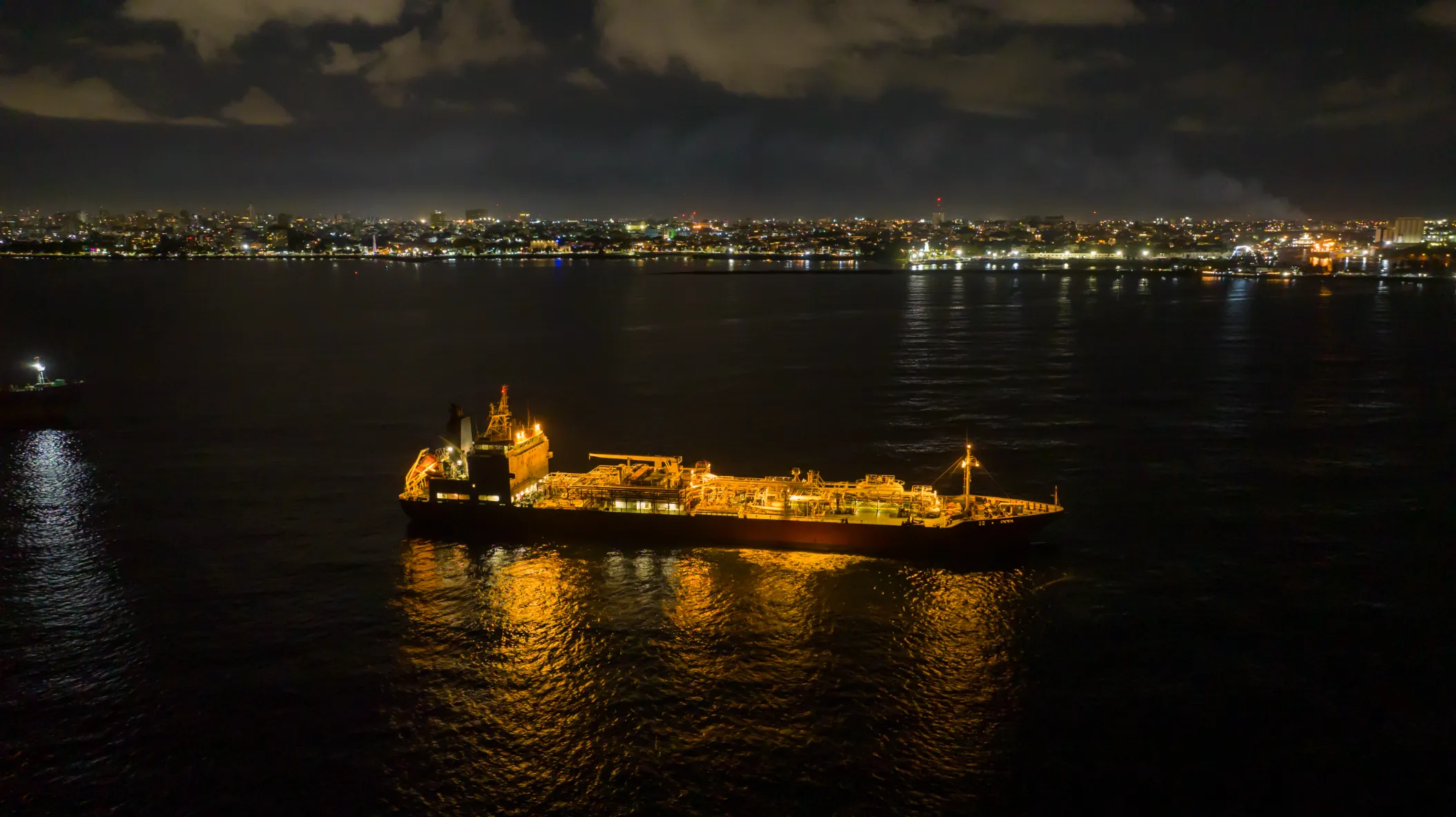 Buque cisterna nocturno en aguas caribeñas Buque cisterna illuminado de noche en el puerto de Santo Domingo, reflejando luz dorada en aguas oscuras del Caribe durante fotografía comercial