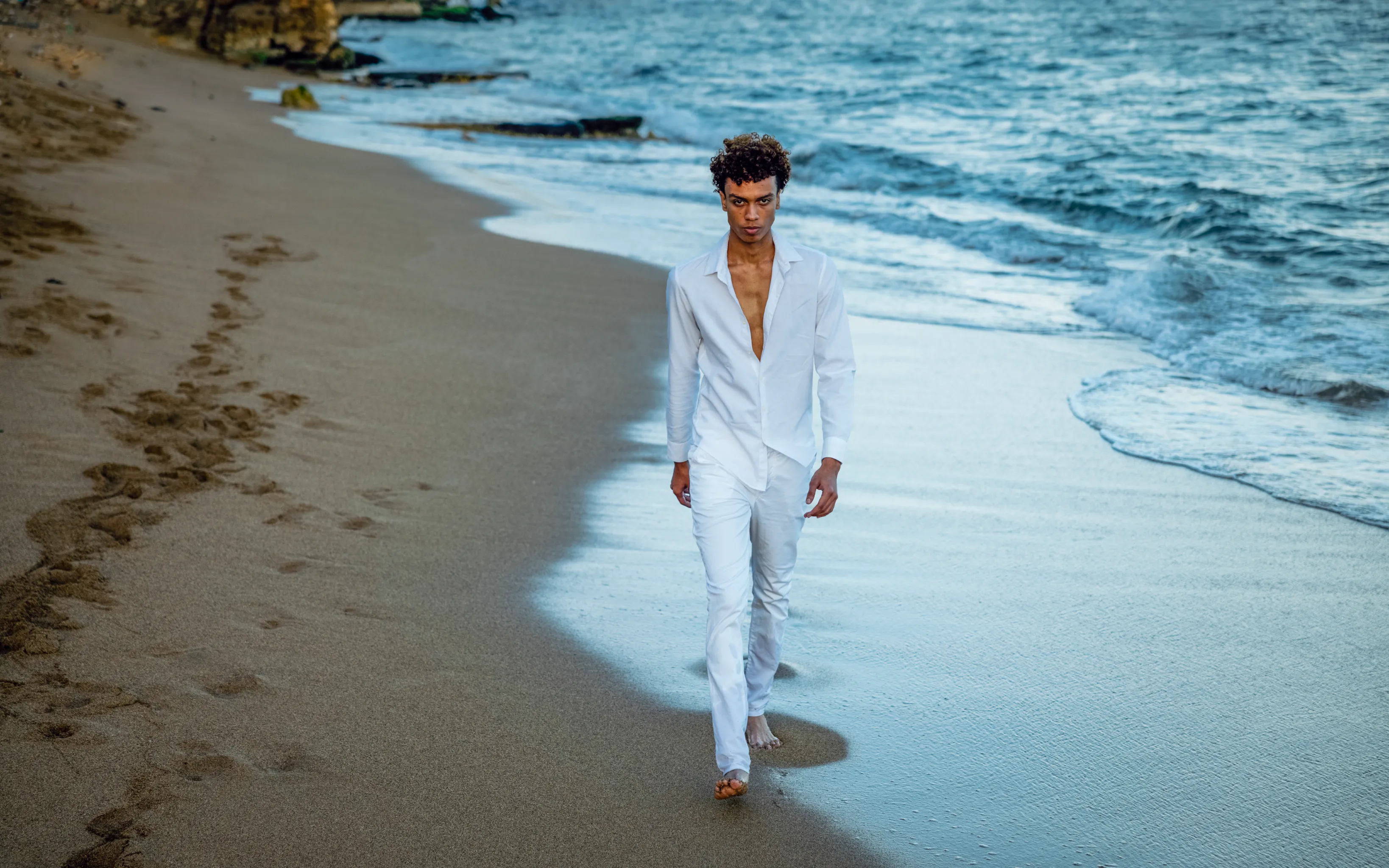 Retrato de moda en arena mojada Hombre en retrato de moda camina descalzo por arena mojada en playa de Santo Domingo, vistiendo lino blanco