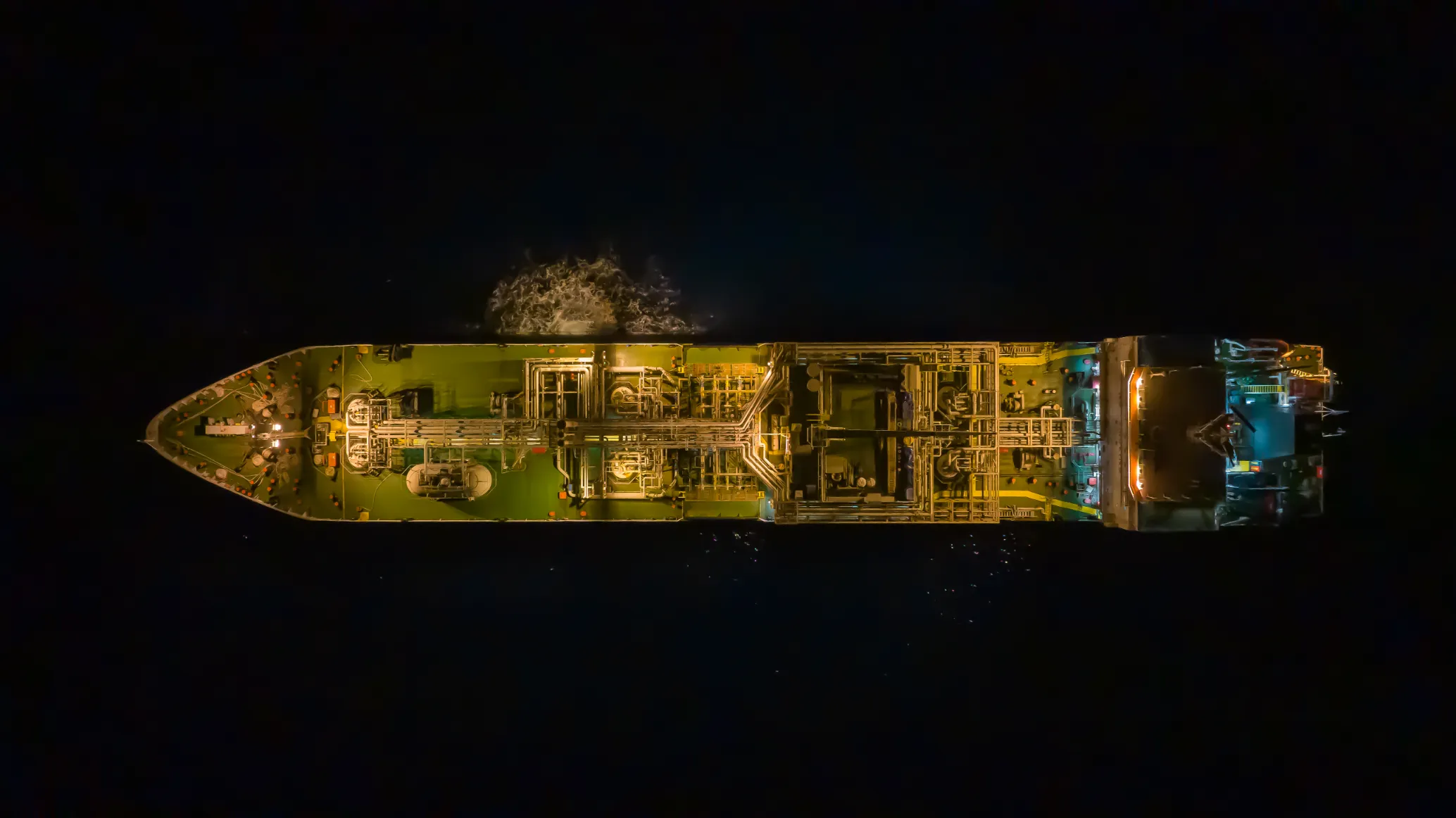 Barco carguero iluminado de noche desde el aire Fotografía aérea nocturna de carguero iluminado en océano oscuro, vista desde drone cenital, luces doradas en cubierta