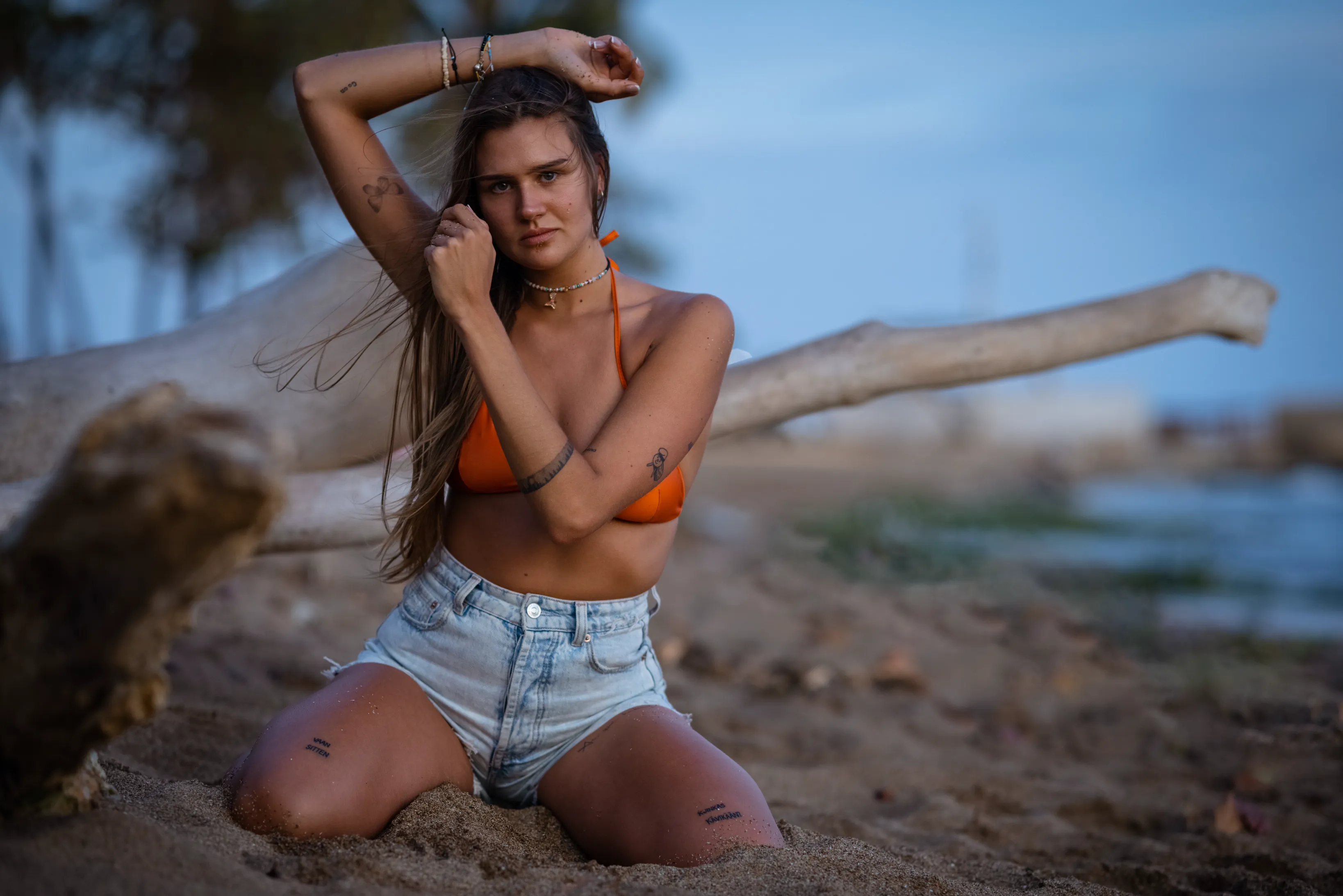 Retrato en playa al atardecer Sesión de retrato de lujo en playa de Santo Domingo: mujer posando en arena junto a madera erosionada con luz dorada del atardecer