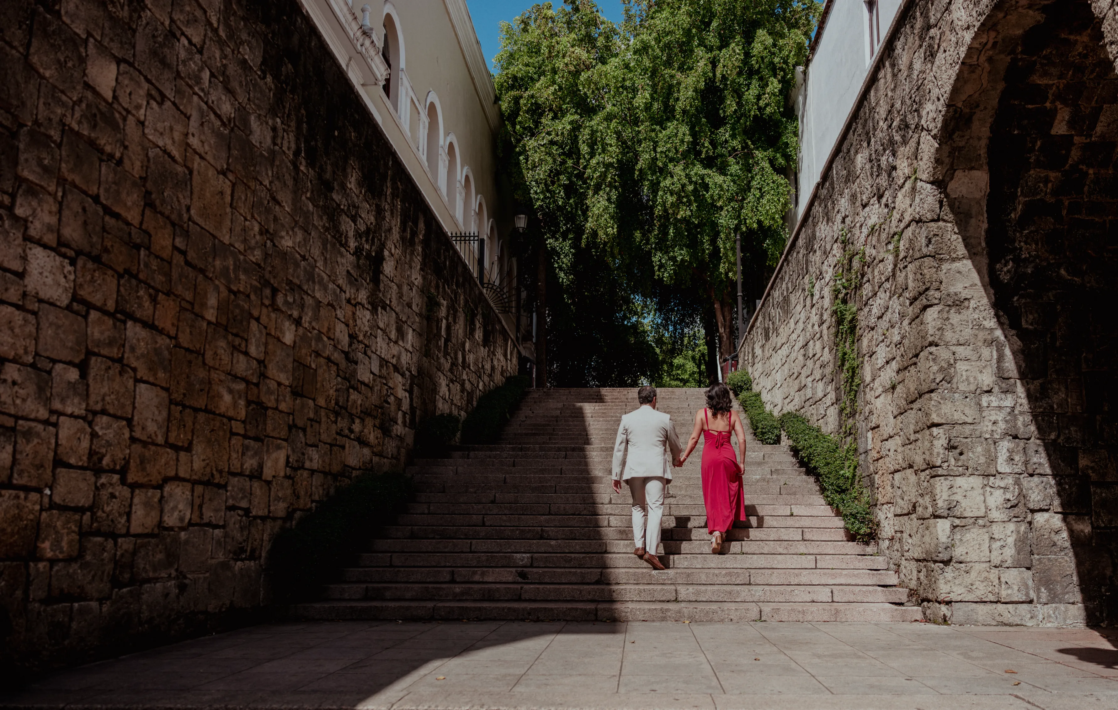 Pareja en escalones coloniales de Santo Domingo Pareja caminando de la mano por escalones coloniales del Centro Histórico de Santo Domingo, ella viste rosa fucsia y él traje claro
