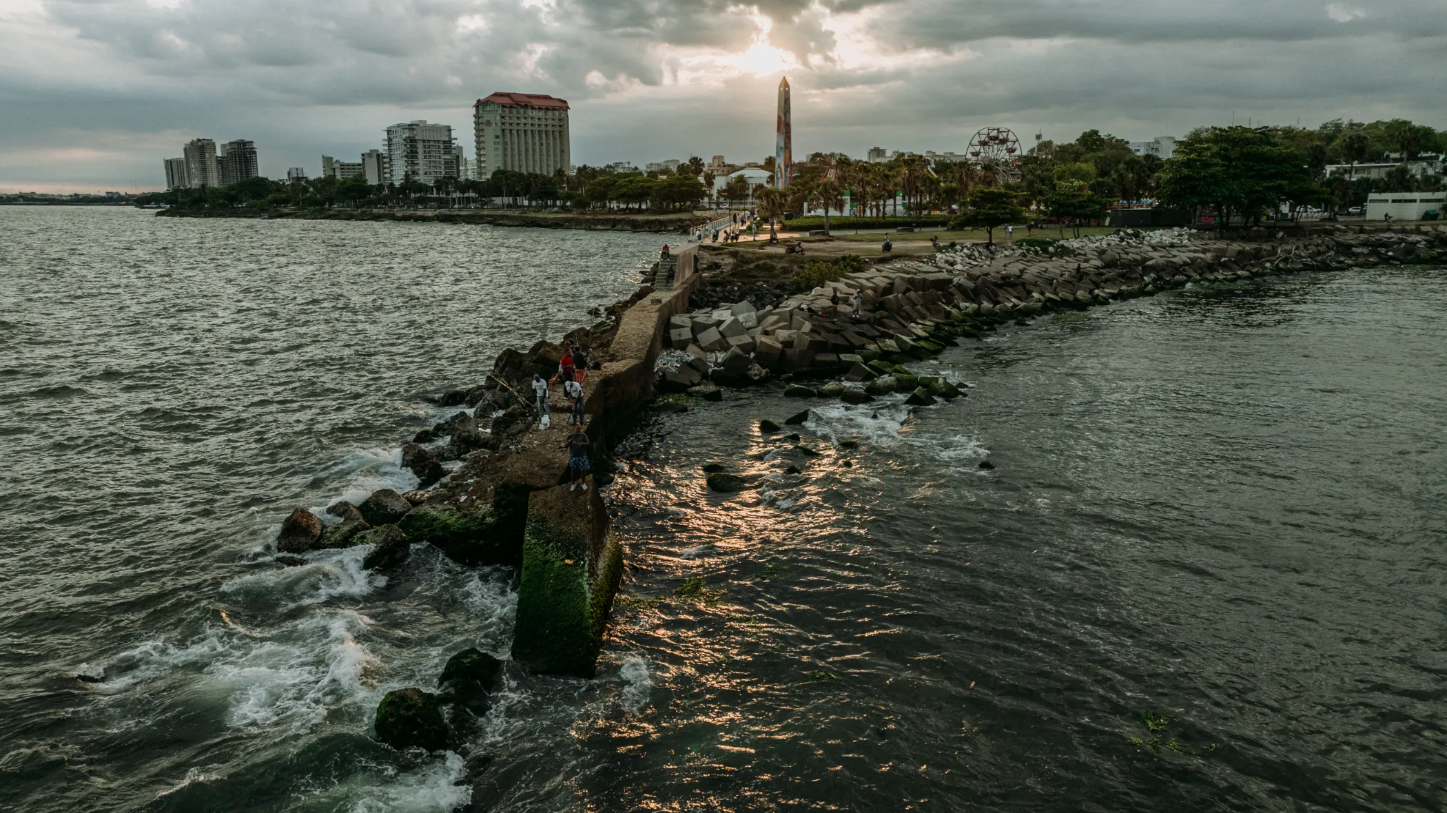 Familia en el espigón del Malecón Familia posando en el espigón del Malecón de Santo Domingo con arquitectura costera y cielo nublado al fondo, sesión de fotografía familiar profesional