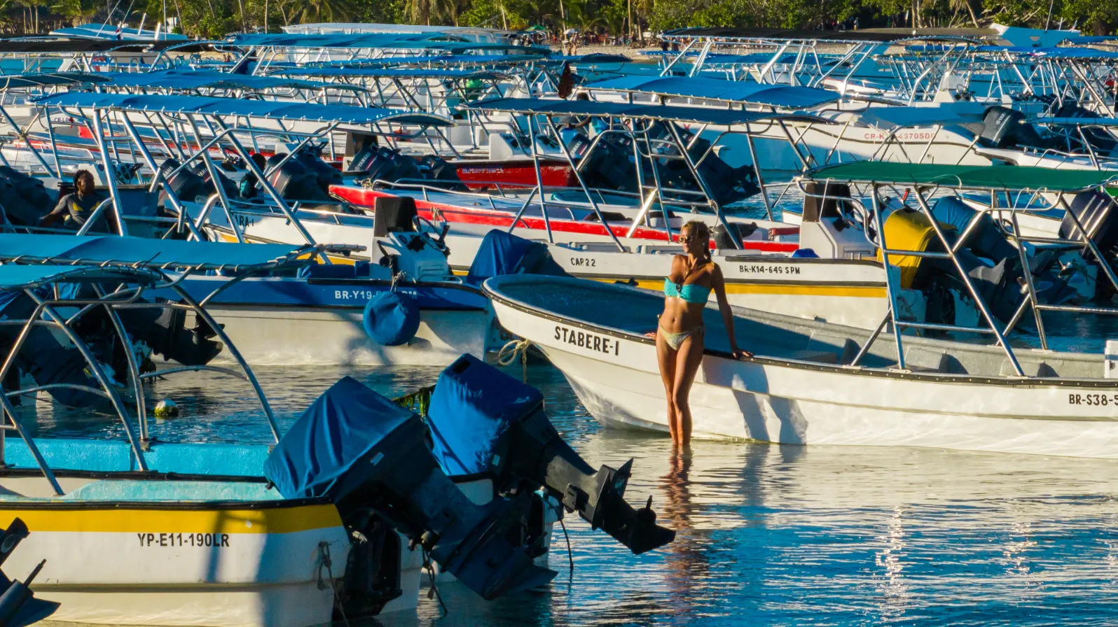 Retrato en el puerto de Samaná Mujer en agua turquesa rodeada de botes azules tradicionales en sesión de playa en Samaná, República Dominicana