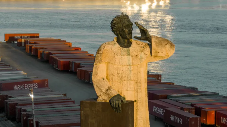 Vigilancia dorada del puerto caribeño Estatua dorada de trabajador observando contenedores de carga al amanecer en puerto de Santo Domingo, fotografía comercial con luz natural.